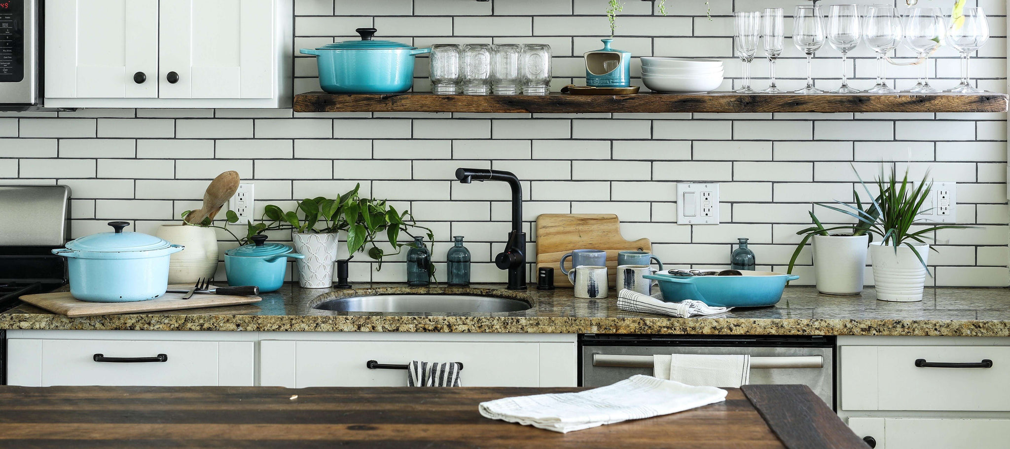 Modern kitchen with white tiled backsplash, wooden countertop, blue cookware, and neatly arranged kitchen towels