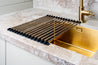 Stainless steel roll-up dish drying rack on countertop near sink.