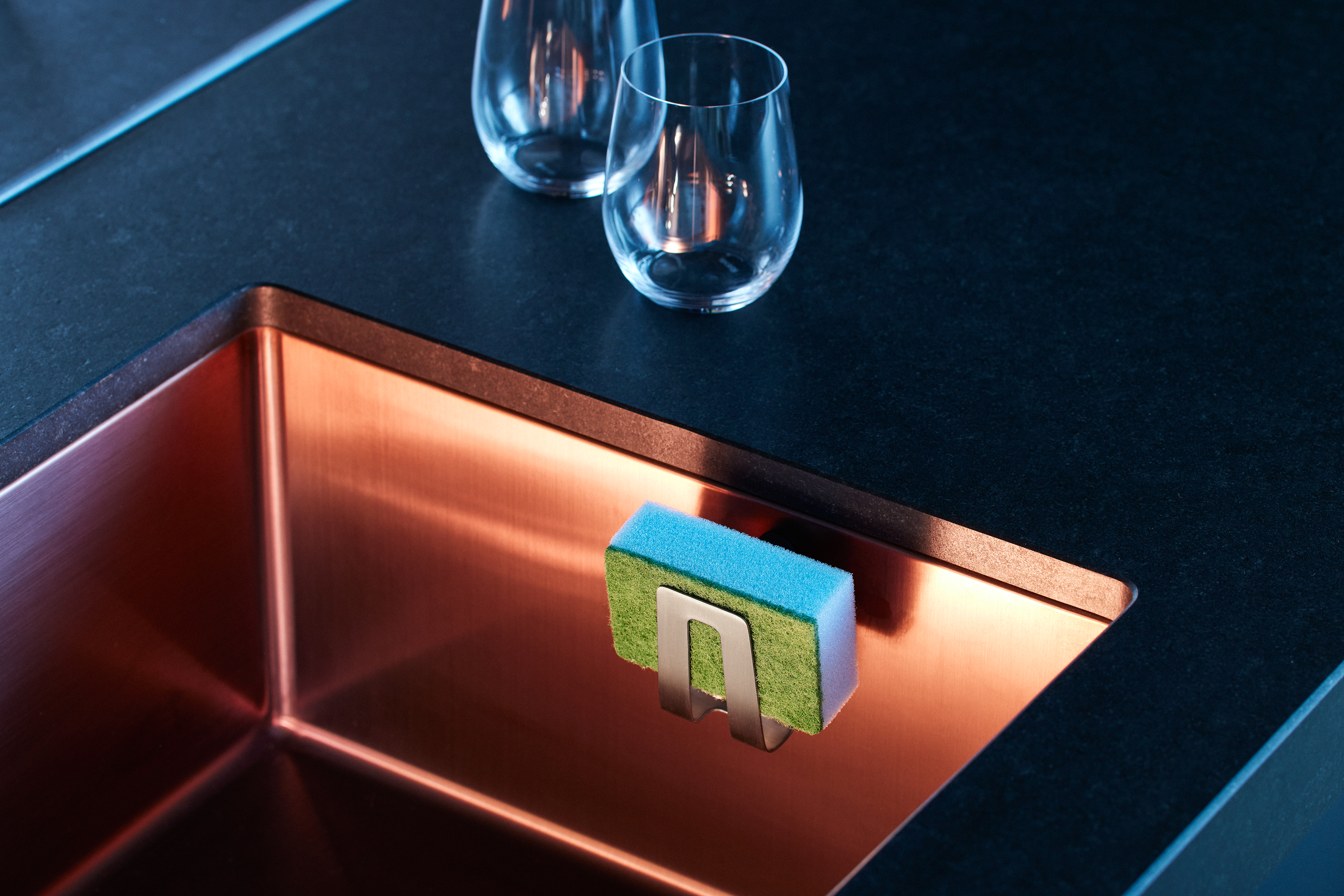 Magnetic sponge holder in steel, attached to a modern kitchen sink for organized sponge storage.