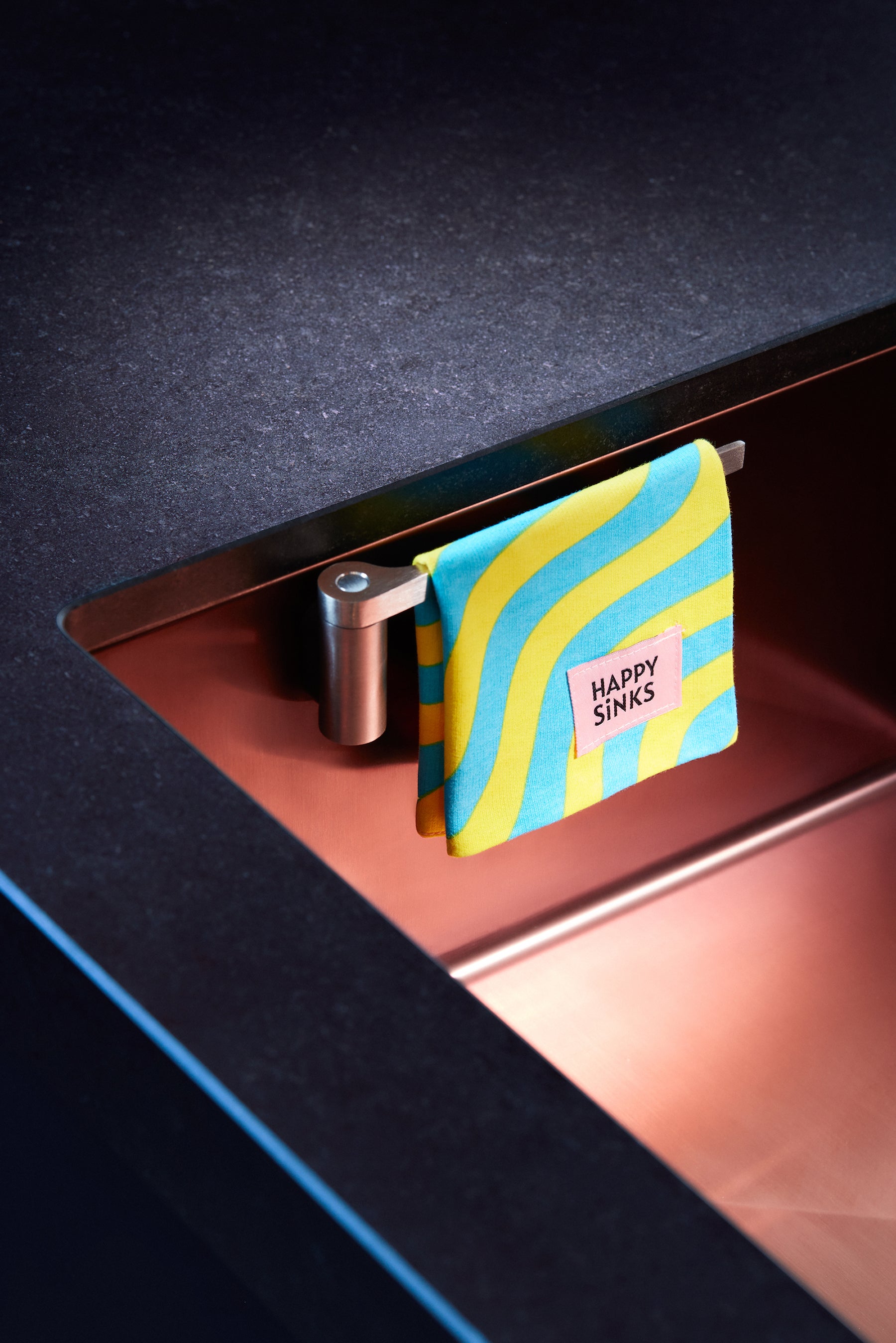 Stainless steel dish cloth holder with colorful cloth in a modern kitchen sink setup.