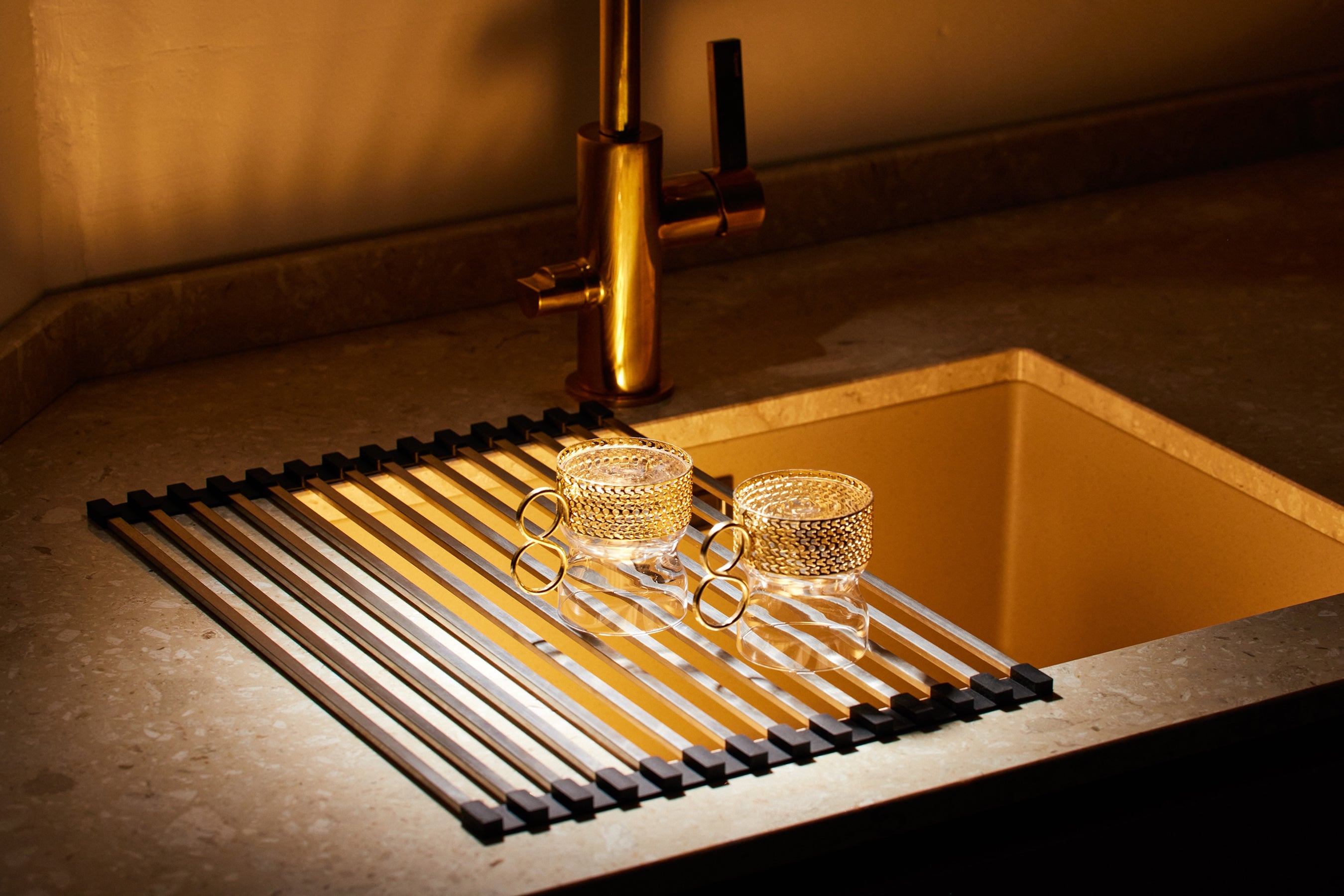 Steel dish drying rack over sink with glasses, space-saving roll-up design.