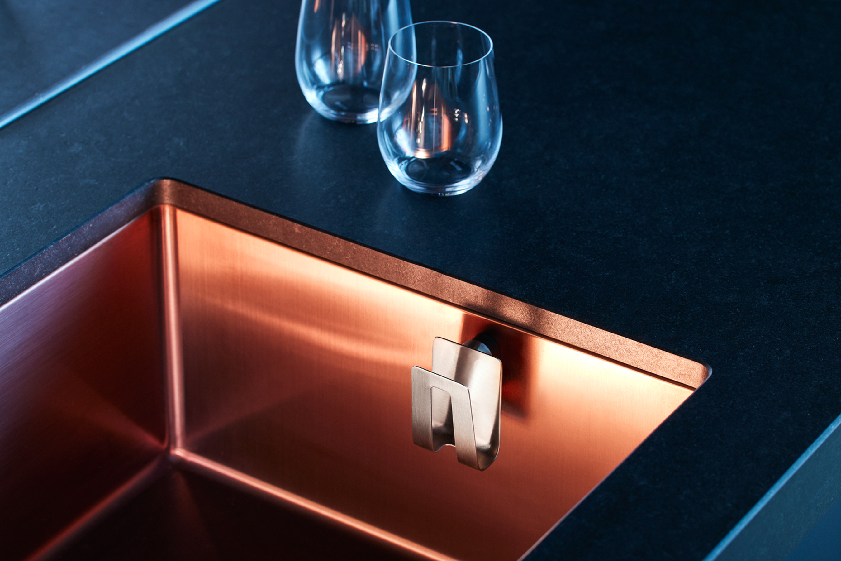 Steel magnetic sponge holder attached to a sink with modern kitchen design.